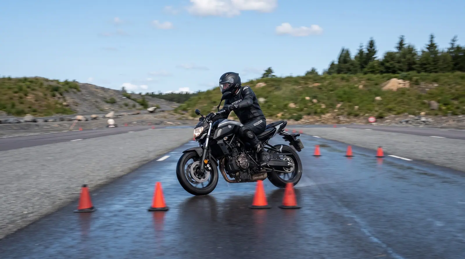 Illustration: motorcyklist i full skyddsutrustning kör mellan koner på halkbanan
